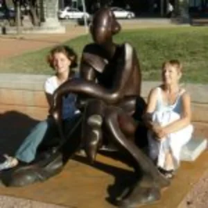Two women seated on a statue, smiling and enjoying their time together in a public space.