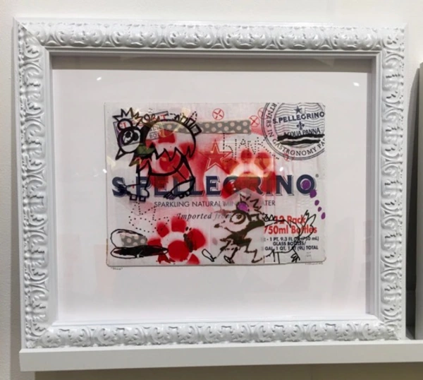 A mixed-media artwork featuring a stylized San Pellegrino label, embellished with colorful graffiti and playful drawings in a white frame.