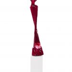 A vibrant red sculpture positioned on a clean white base, showcasing a modern artistic design.