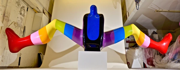 A colorful art piece featuring a glossy black torso with vibrant, striped legs in red, pink, yellow, green, blue, and purple.
