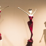 Three sculptures of women in red and white, elegantly posed on pedestals, showcasing artistic expression and form.