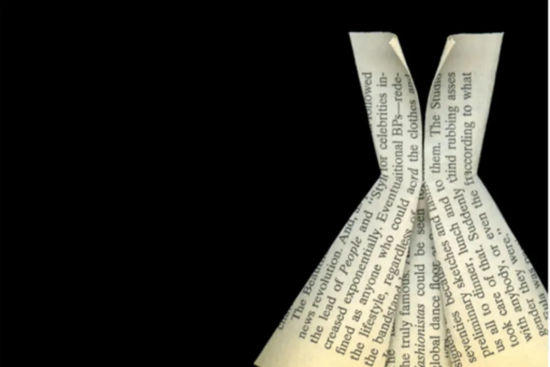 Close-up of a folded paper resembling a dress, with printed text visible, against a black background.
